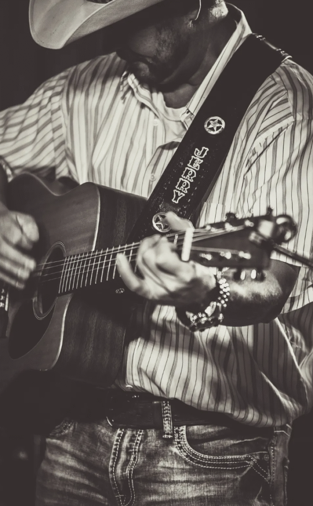 image of musician Jerry Schmitt wearing a cowboy hat, long sleeve shirt, and jeans. he is playing an acoustic guitar.